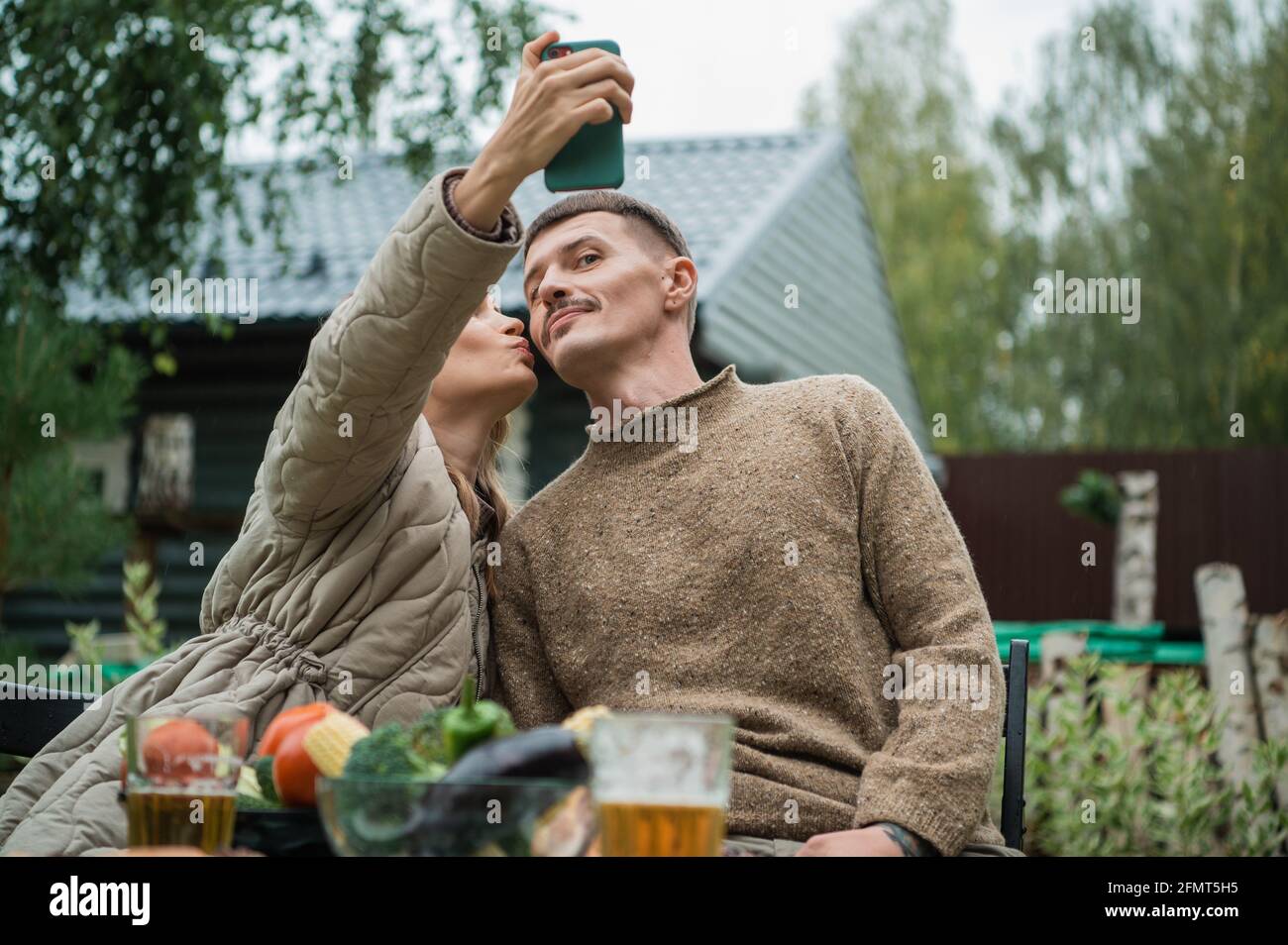 Ein junges Paar macht ein sehr lustiges und emotionales Selfie, täuscht sich herum und macht Gesichter vor der Smartphone-Kamera. Sie machten ein Abendessen im Freien Stockfoto