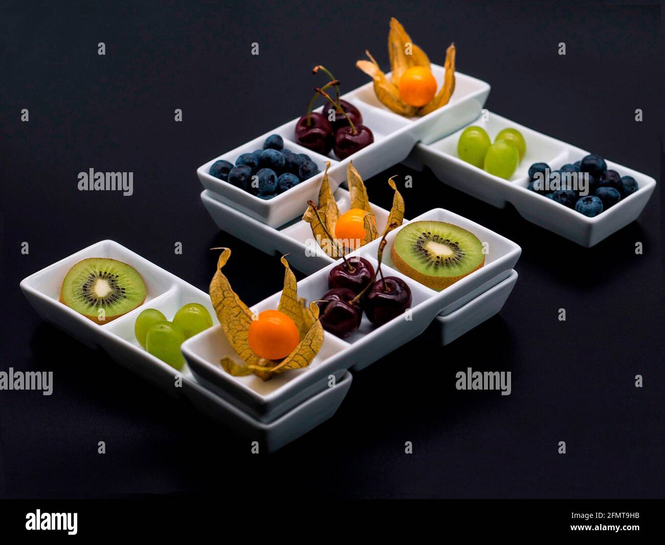 „Five a Day“ ist eine Auswahl von 5 frischen, gesunden Früchten, die auf einzigartige Weise in 5 weißen Porzellanschalen präsentiert werden, die eine Fünffache bilden. Schwarzer Hintergrund Stockfoto