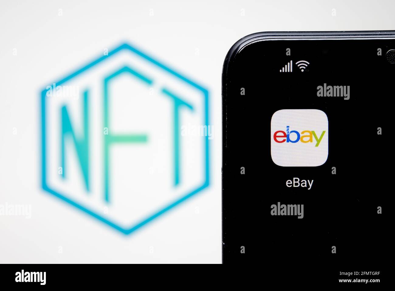 EBAY NFT-Konzept. EBay-App auf dem Smartphone und verschwommenes nicht fungible Token-Logo auf dem verschwommenen Hintergrund Laptop-Bildschirm. Stafford, Großbritannien Stockfoto