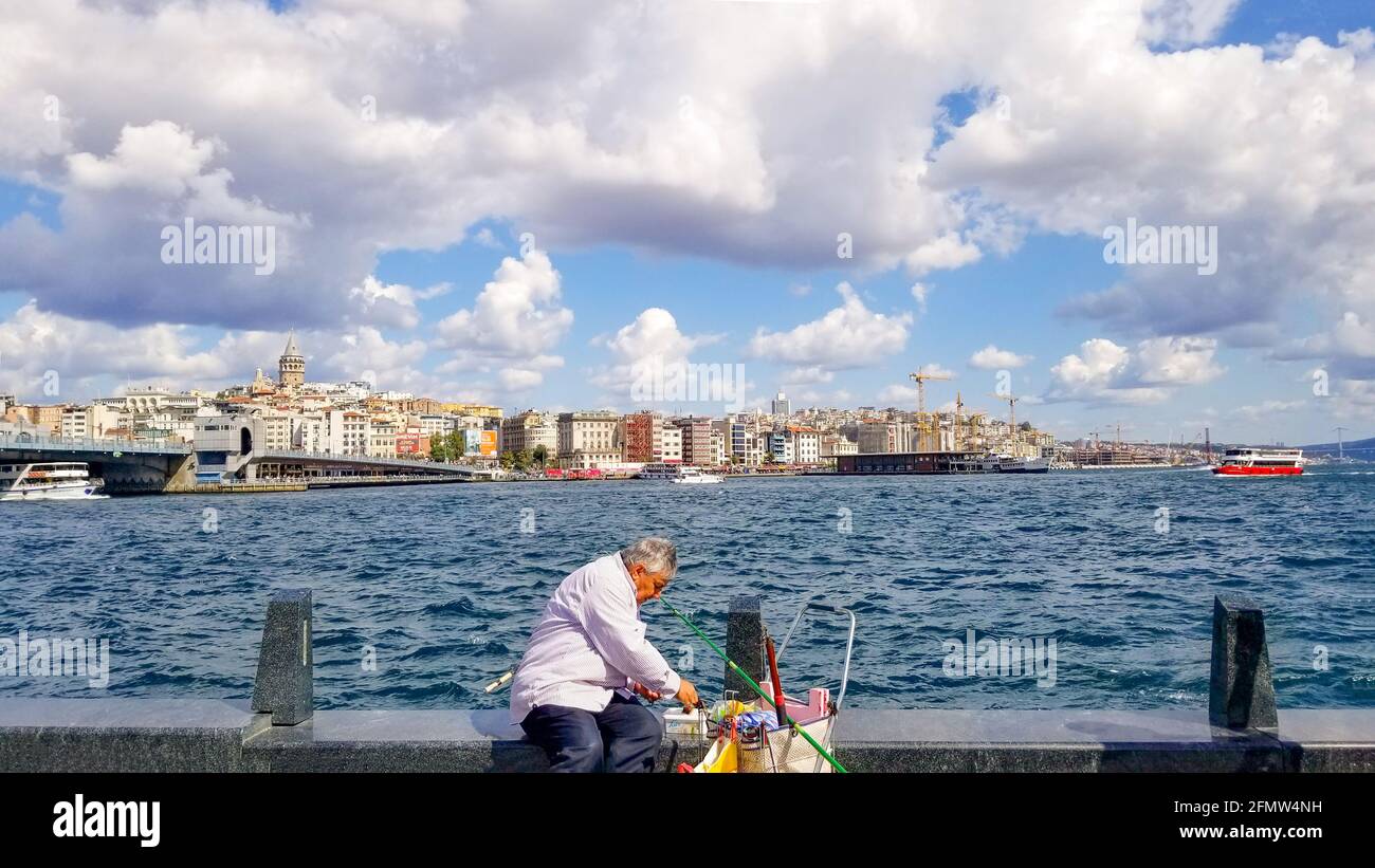 Ein türkischer Fischer mit Tackle Box, Angelschnur und Stange wird loswerden, um im Bosporus-Fluss mit dem Galata-Turm hinter sich in der Türkei in Istanbul zu fischen. Stockfoto