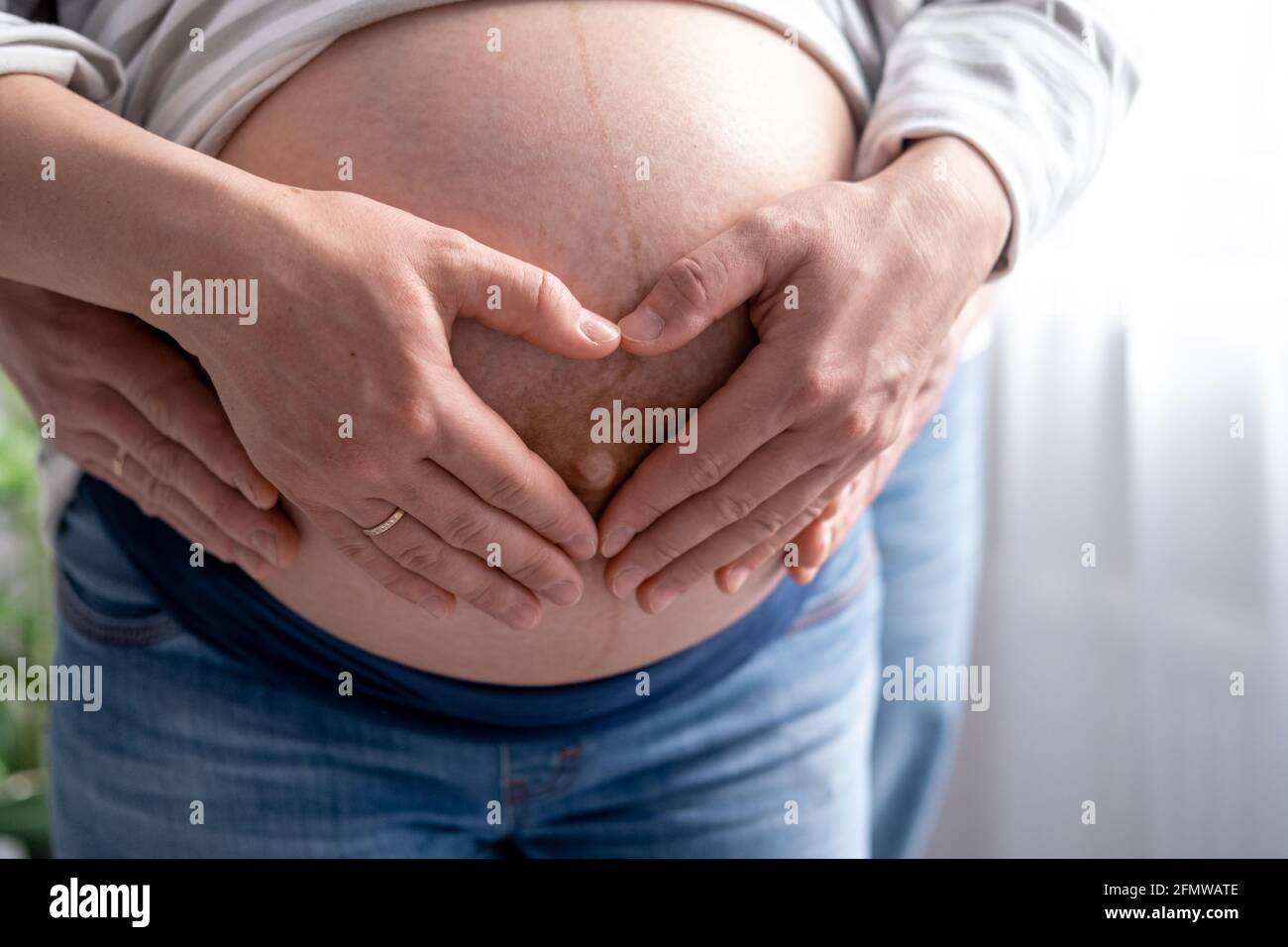 Nahaufnahme Hände auf Mutter und Vater Herz auf schwanger großen Bauch fortgeschrittenen Schwangerschaft. Geliebte Eltern warten Baby Familie Schwangerschaft. Stockfoto