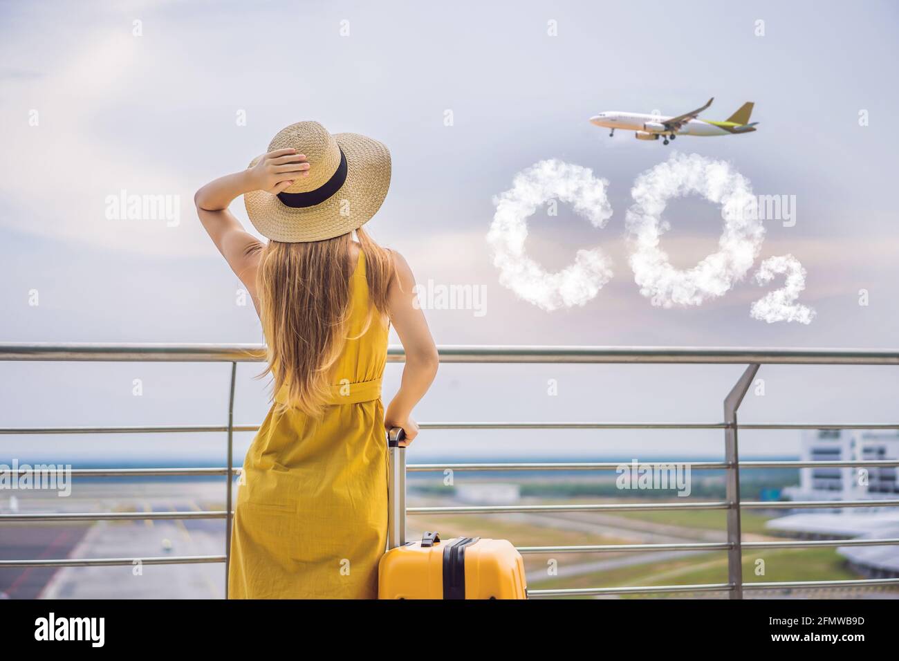 Schöne junge Frau lTraveler in einem gelben Kleid und einem gelben Koffer  wartet auf ihren Flug CO2-Schriftzug aus Wolken. Himmel mit  CO2-Verschmutzung Stockfotografie - Alamy