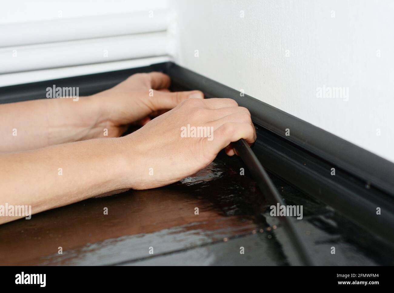 Ein Mann installiert eine schwarze Kunststoff-Sockelleiste, um Kabel und Drähte zu verbergen. Ein Hausbesitzer verbirgt die Verkabelung im Kabelkanal einer Sockelleiste. Stockfoto