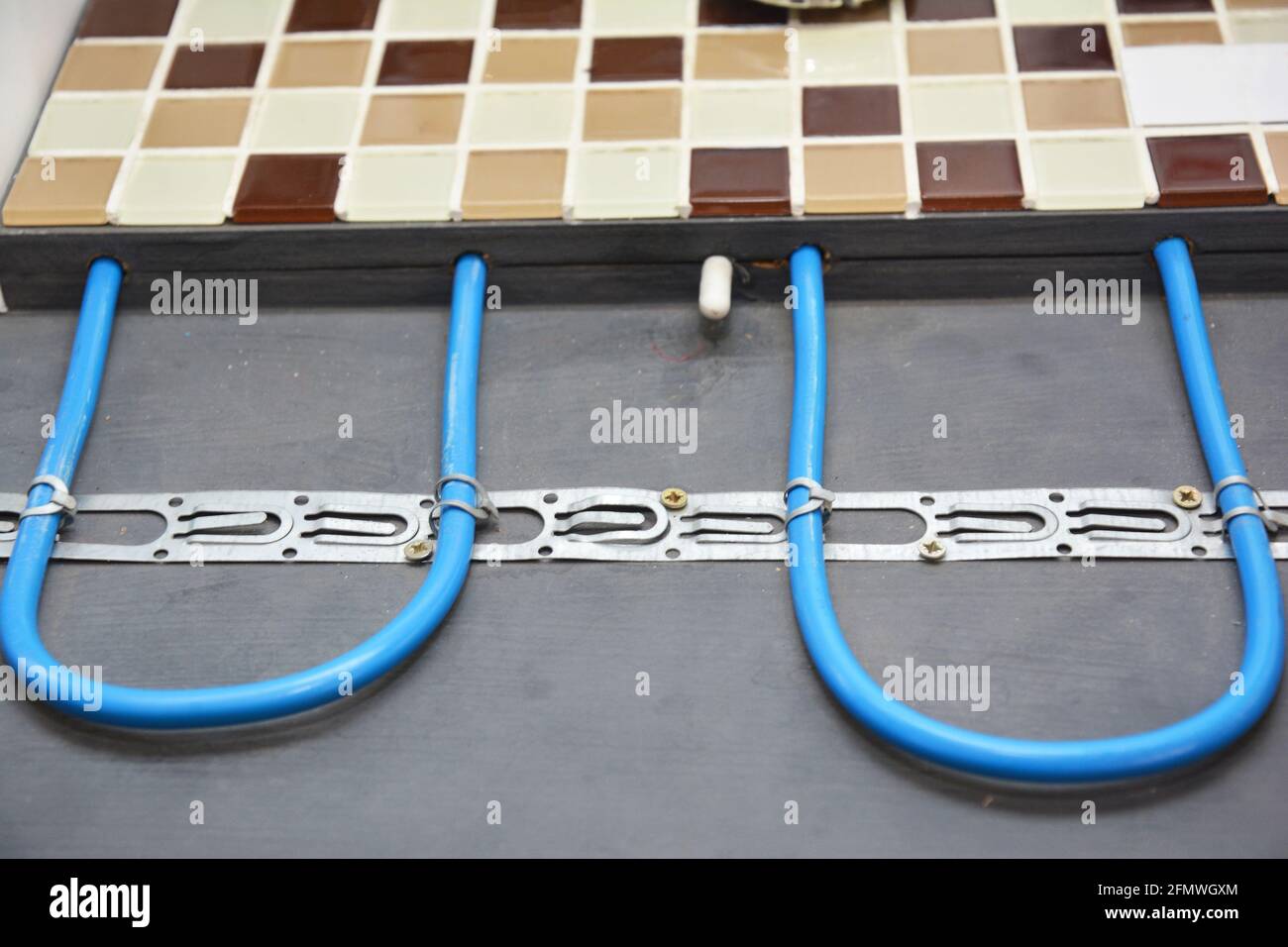 Elektrische Fußbodenheizung Installation: Nahaufnahme einer elektrischen Fußbodenheizung, die mit Mosaikfliesen im Badezimmer bedeckt ist. Stockfoto