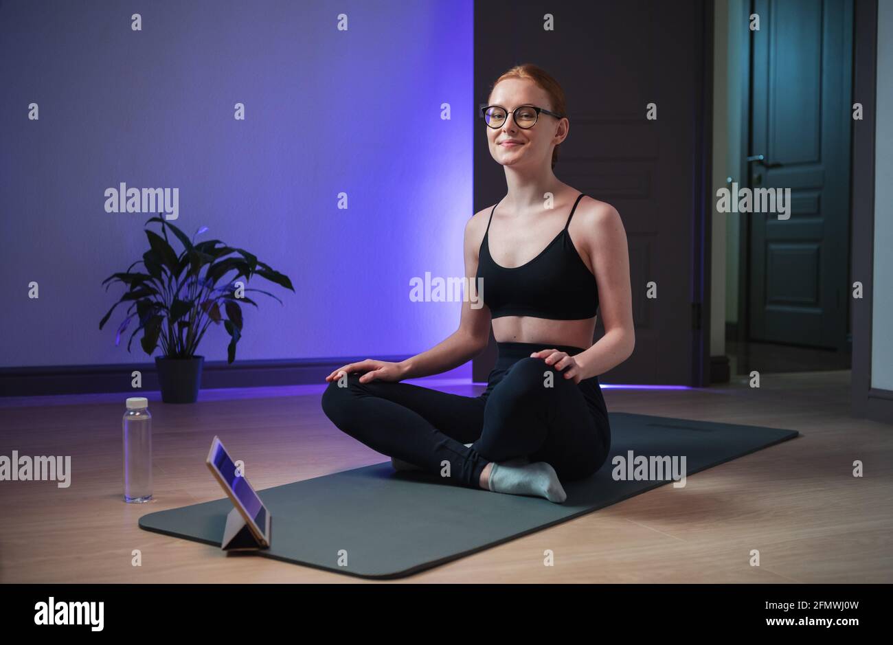 Nettes Mädchen lindert Stress zu Hause mit Yoga, sie schaut sich die Meditationsanleitung auf der Tablette an und beruhigt sich. Stockfoto