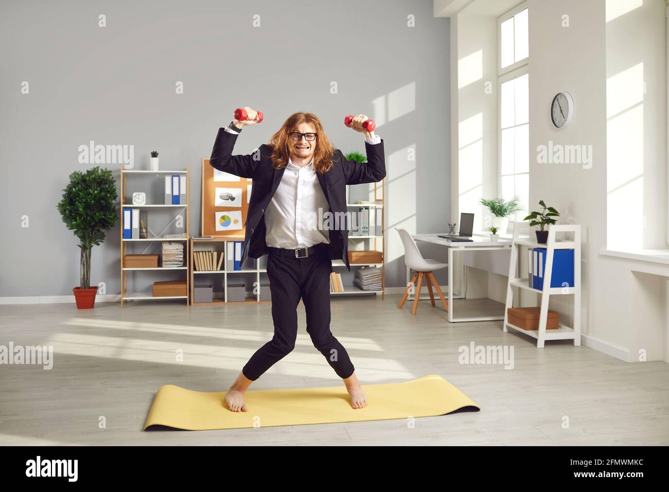 Lustige Arbeiter tun Fitness-Übung mit Hanteln während des Arbeitstages Im Büro Stockfoto