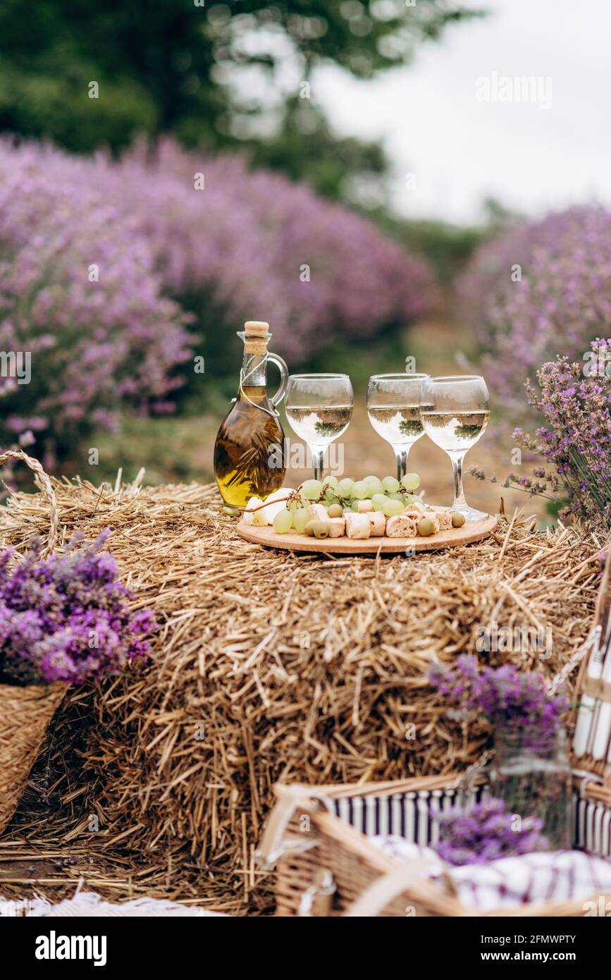 Sommerpicknick im Lavendelfeld. Gläser Wein, ein Picknickkorb, Snacks und Blumensträuße auf einem Heuhaufen zwischen den Lavendelbüschen. Weiches se Stockfoto