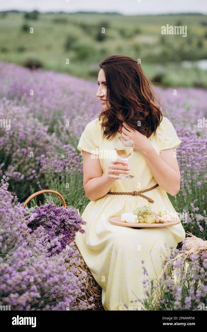 Junge schöne Frau in Kleid mit einem Glas Wein in einem Lavendelfeld. Weicher, selektiver Fokus, Bildrauschen Stockfoto