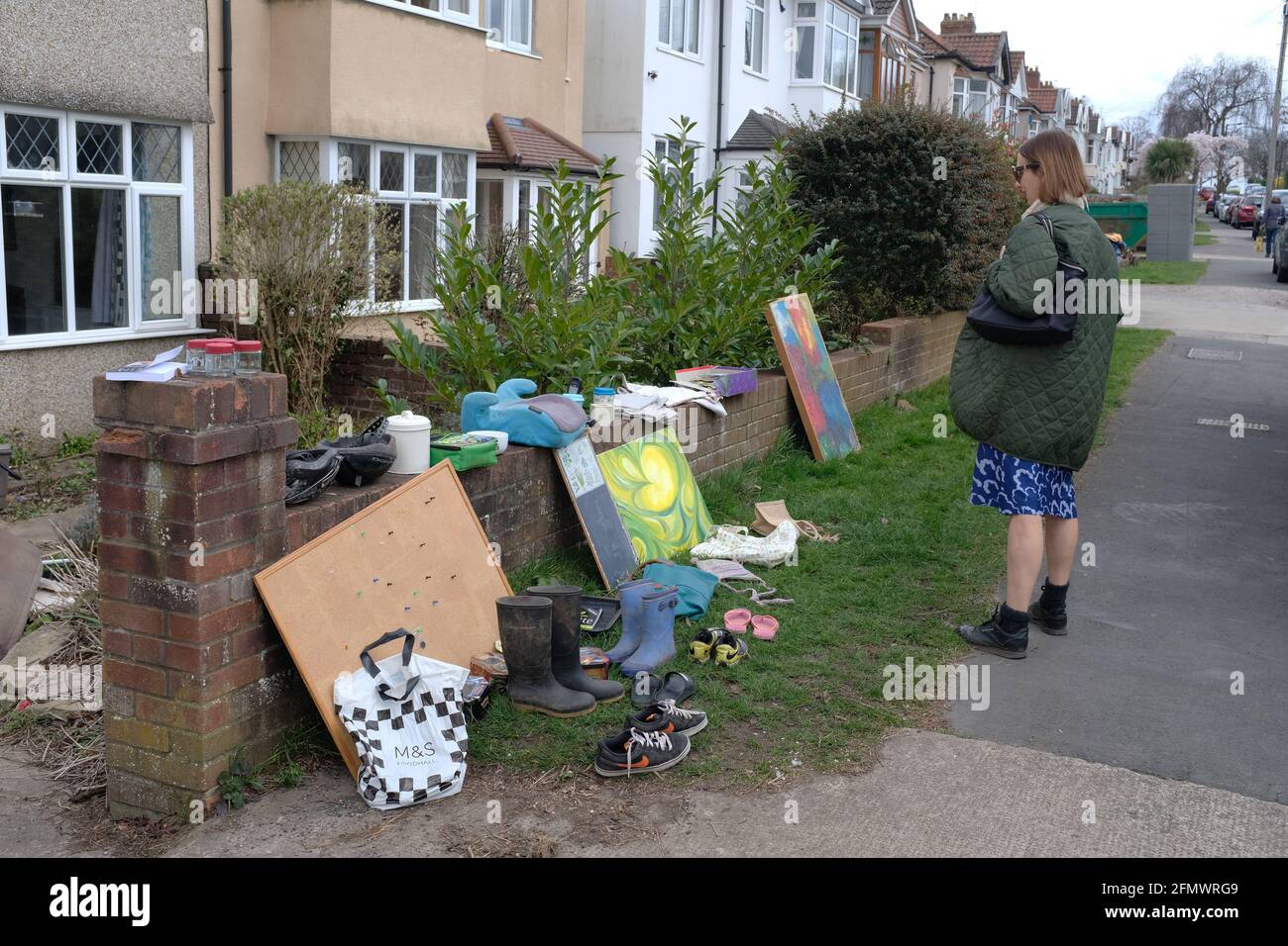 Eine Frau, die alte Dinge betrachtet, die vor einem Haus zurückgelassen wurden, um sie wegzunehmen. Stockfoto