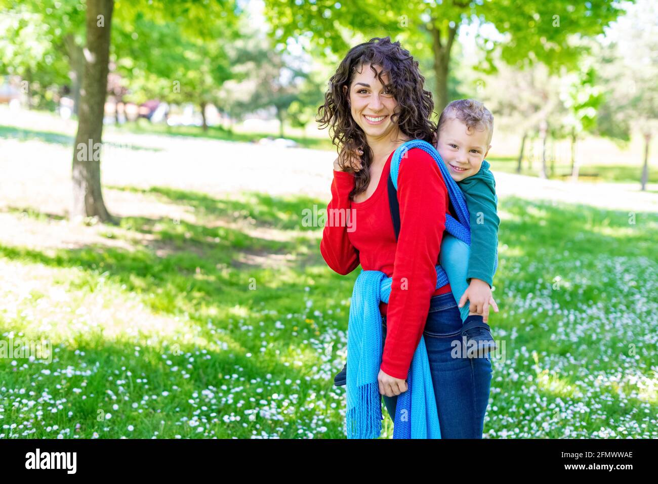 Glückliche junge Mutter trägt ein Kind auf ihrem Rücken, gefesselt Mit  einem farbenfrohen traditionellen Stoffstück in der Öffentlichkeit park  Garden.Mutter und Sohn in einem Babywickel Stockfotografie - Alamy