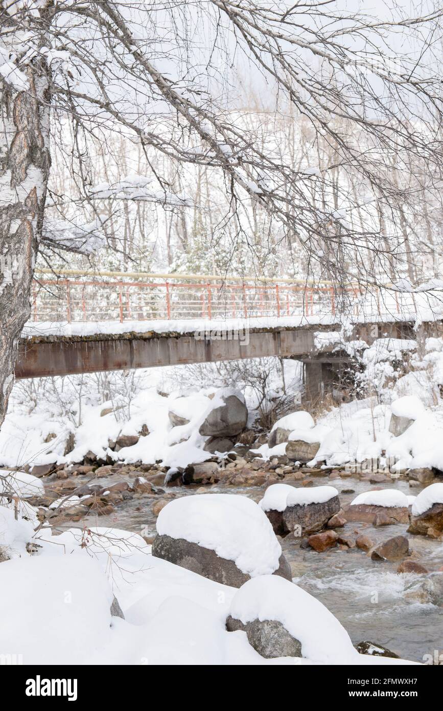 Eine Brücke über einen Gebirgsfluss im Schnee Stockfoto