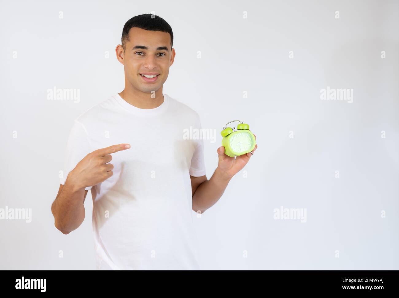 Lächelnder junger Mann, der einen Wecker auf weißem Hintergrund hält. Stockfoto