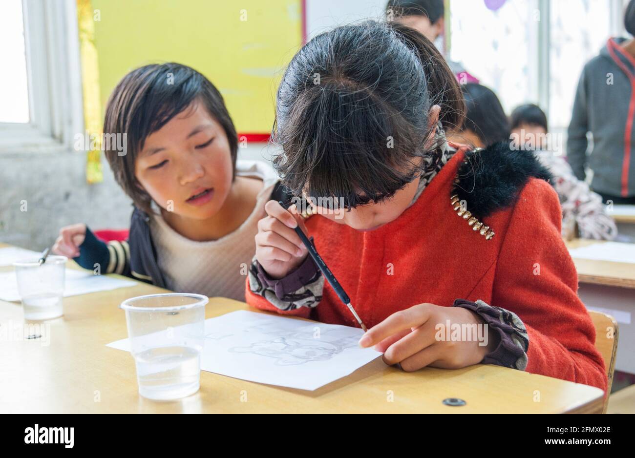 Grundschüler genießen ihr Malen mit Wasser in einer ländlichen Schule in China. Stockfoto