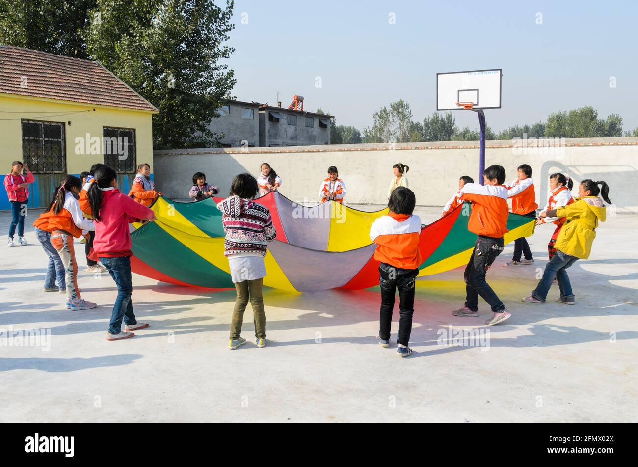 Grundschüler, die während einer Sportklasse mit einem Fallschirm spielen. Stockfoto