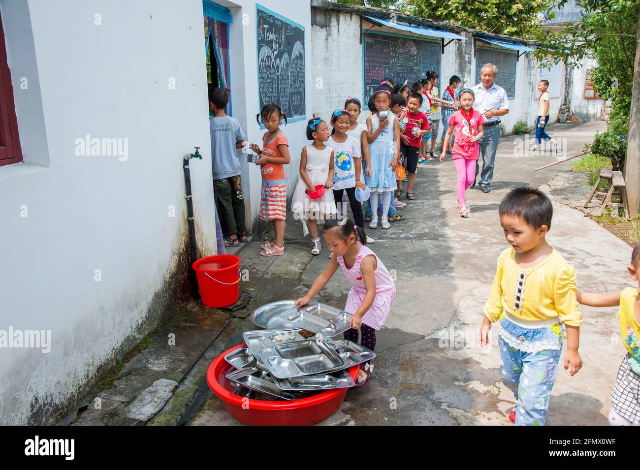 Schüler, der sich zum Mittagessen anstellt und Teller in einer ländlichen Schule in Xiuning, Anhui, China, zurückgibt Stockfoto