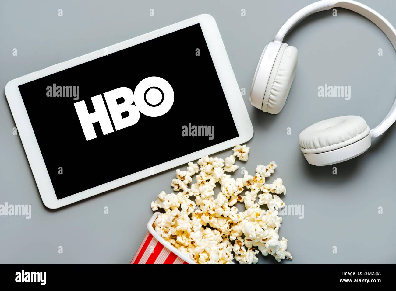 HBO-Logo auf dem Bildschirm eines weißen digitalen Tablets Mit Popcorn und weißen Kopfhörern auf grauem Hintergrund Stockfoto