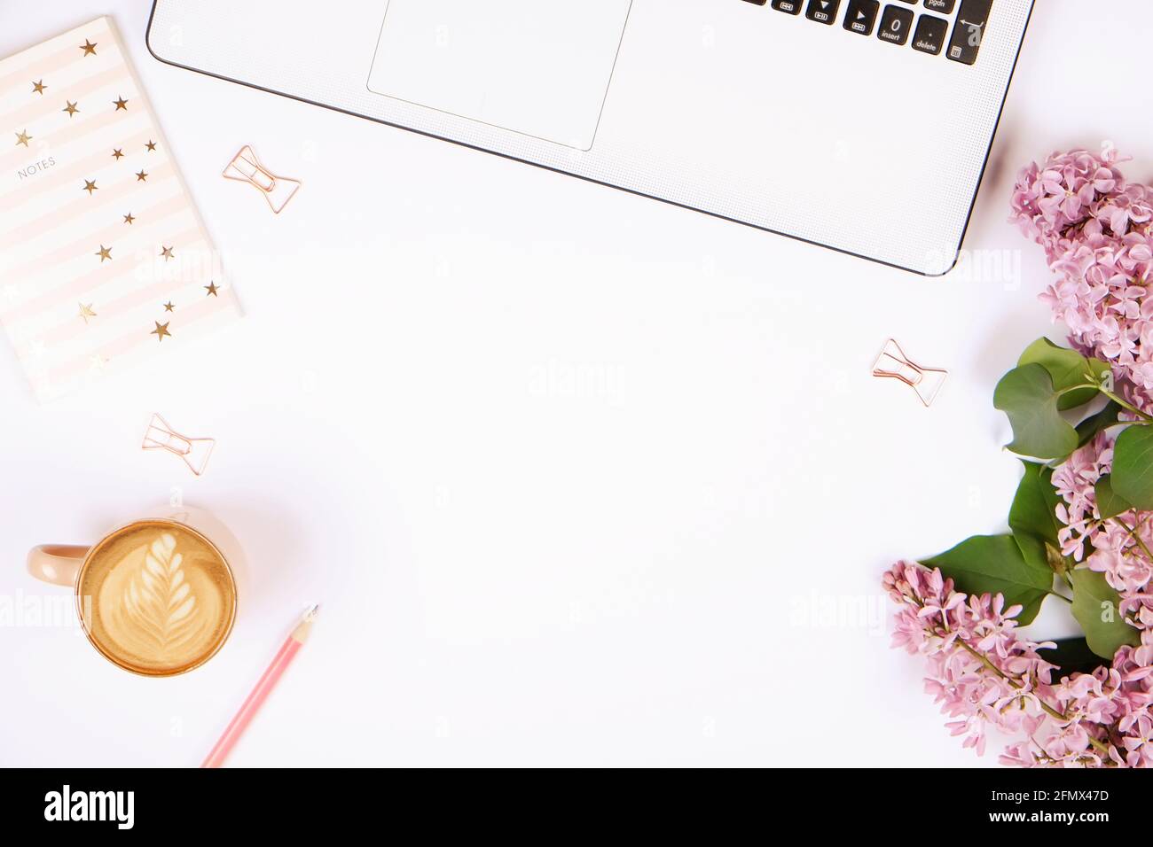 Feminine Nahaufnahme des Desktops, Laptop-Computertastatur, Tasse Kaffee mit Latte Art, lila Blumen. Minimal beschnittene flache Lay-Komposition, Notizbuch, cbc Stockfoto