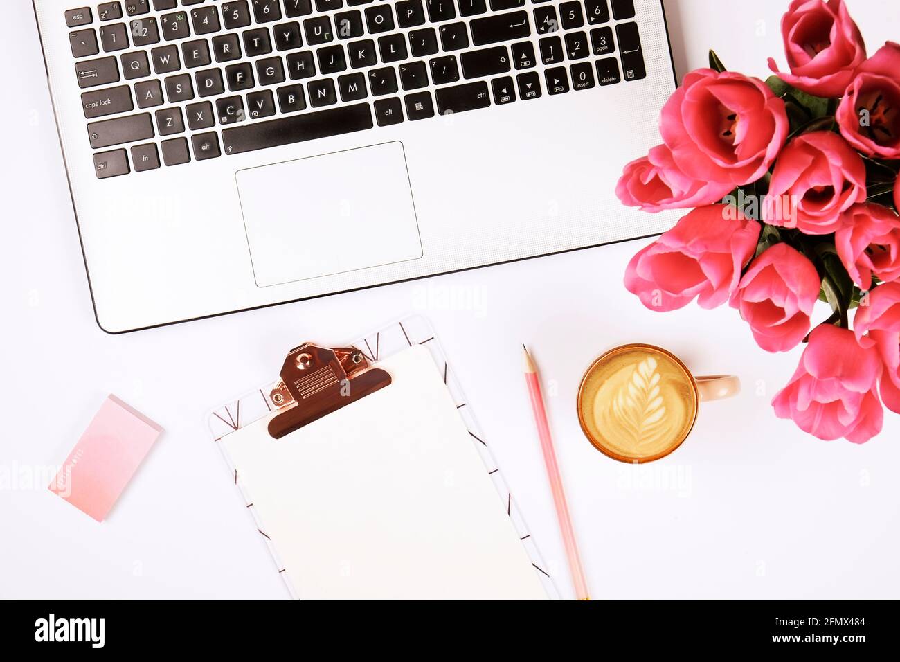Feminine Nahaufnahme der Laptop-Computer-Tastatur, Kaffeetasse und rosa Tulpenblüten. Flache Lay-Komposition mit Notizbuch, leeres Blatt-Clipboar Stockfoto