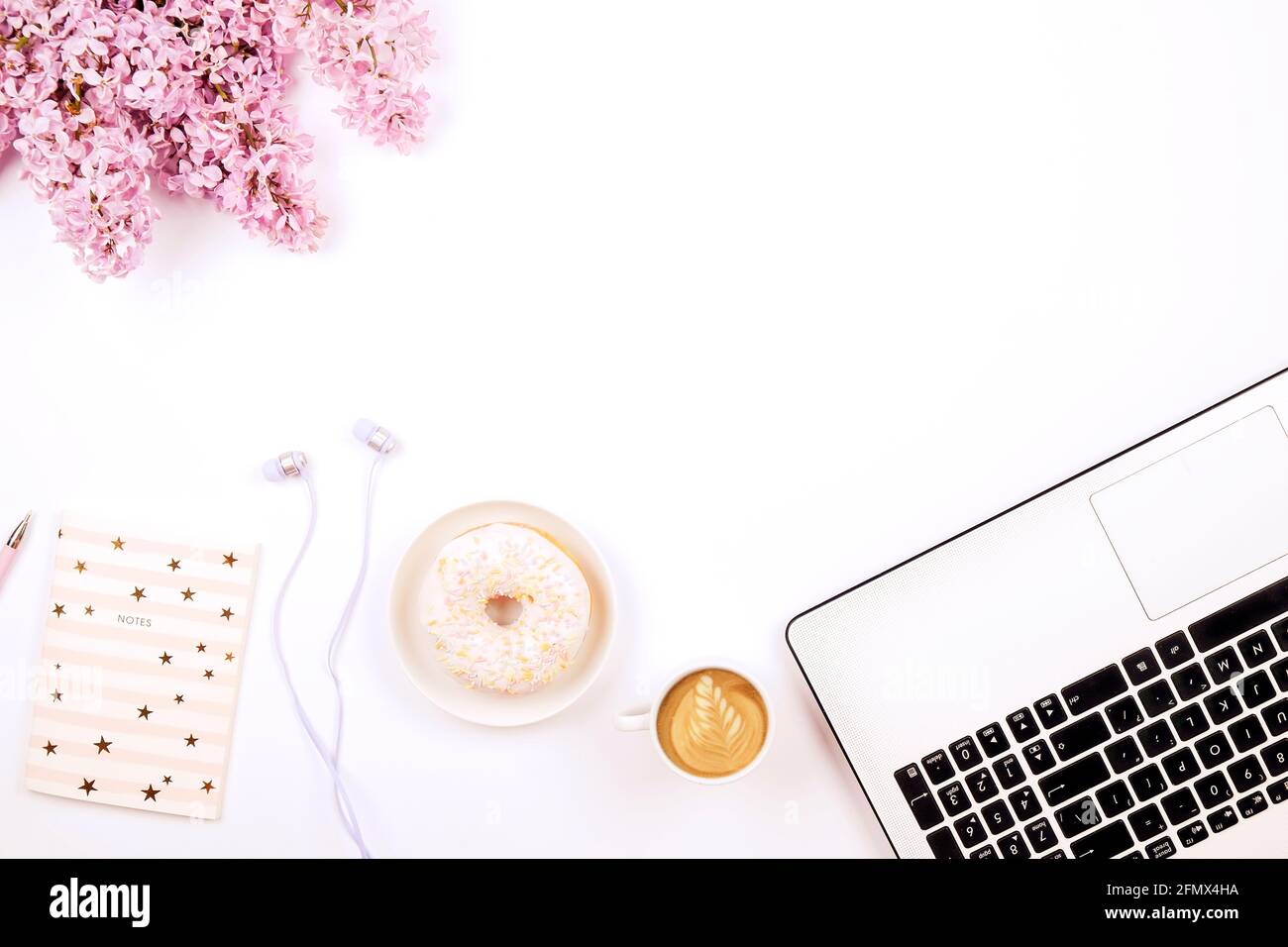 Feminine Nahaufnahme des Desktops, Laptop-Computertastatur, Tasse Kaffee und Donut, lila Blumen. Minimal beschnitten flach Lay Zusammensetzung, Notizbuch, Cappuccin Stockfoto