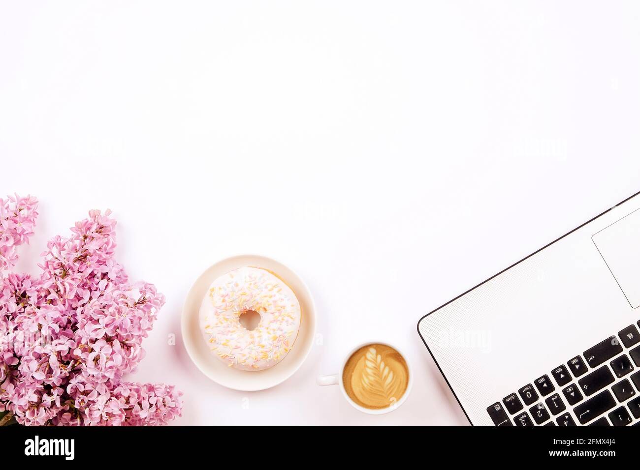 Feminine Nahaufnahme des Desktops, Laptop-Computertastatur, Tasse Kaffee und Donut, lila Blumen. Minimal beschnitten flach Lay Zusammensetzung, Notizbuch, Cappuccin Stockfoto