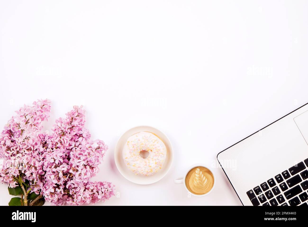 Feminine Nahaufnahme des Desktops, Laptop-Computertastatur, Tasse Kaffee und Donut, lila Blumen. Minimal beschnitten flach Lay Zusammensetzung, Notizbuch, Cappuccin Stockfoto