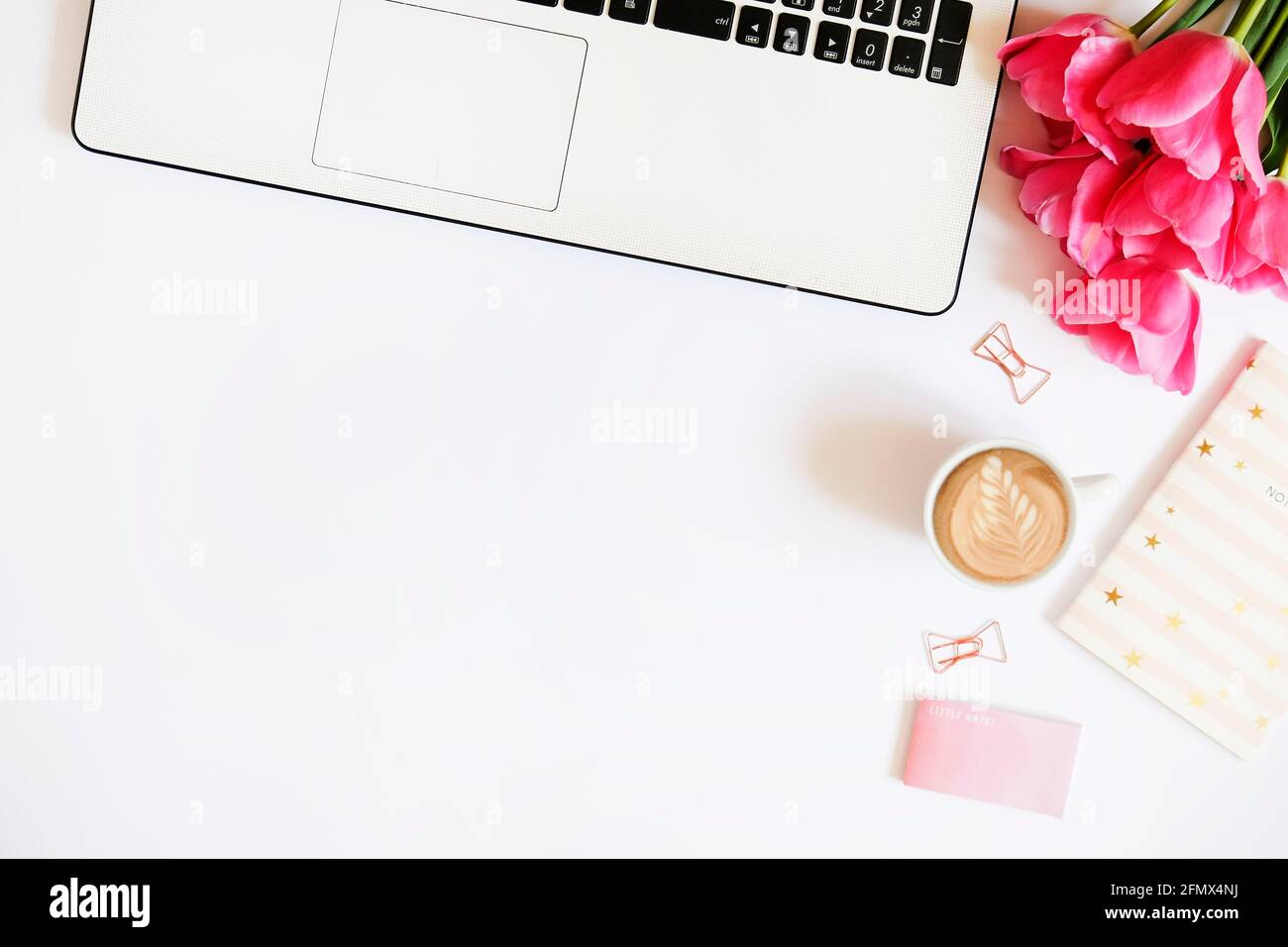Femininer Büro-Desktop mit schwarz-weißer Laptop-Tastatur, rosa Tulpenblüten-Bouquet, Tasse Kaffee mit Latte Art, Stift, Notebook-Computer, verschiedene Su Stockfoto