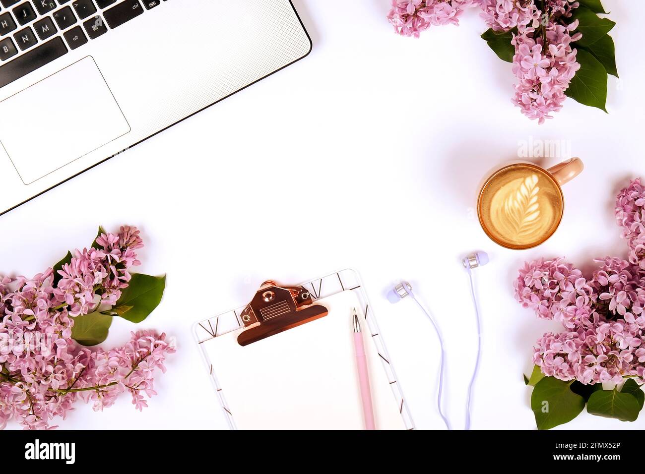 Feminine Nahaufnahme der Laptop-Computer-Tastatur, Kaffeetasse und lila Blumen. Flache Lay-Komposition mit Notizbuch, leerem Blatt-Klemmbrett, Kopfhörer, Stockfoto