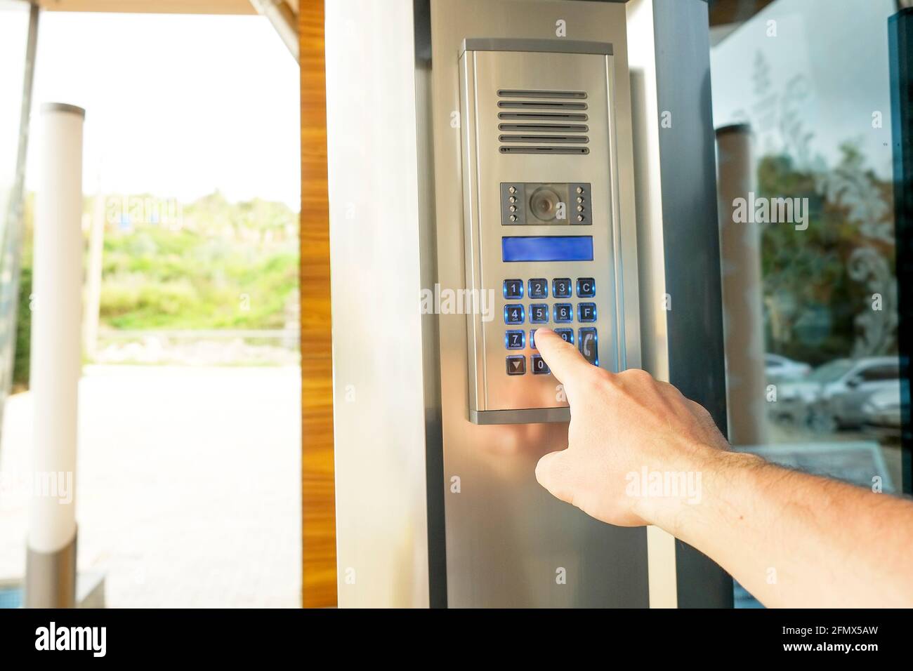 Nahaufnahme der Hand des Mannes Eingabe von Sicherheits-System-Code, Drücken der Taste mit Zeigefinger auf moderne Gegensprechanlage mit blauem lcd-Bildschirm in der Nähe Eingang doo Stockfoto