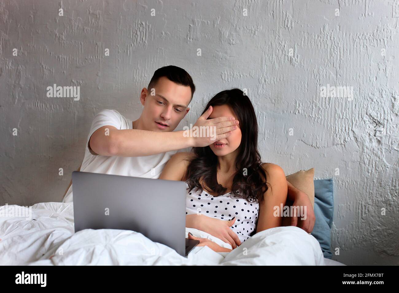 Paar im Bett mit Laptop. Junge amerikanische Männer und Frauen, Ehemann und Ehefrau, die sich verliebt haben, einen starrenden pc-Notebook-Computer zu halten. Männliche und weibliche Modell Surfen Surfi Stockfoto