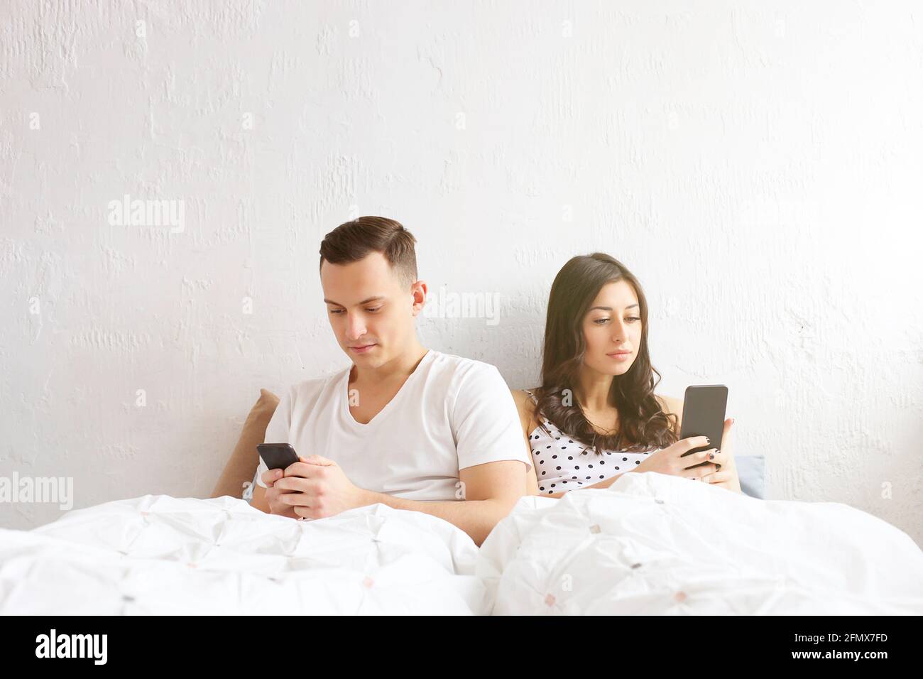Junge amerikanische Männer und Frauen, die auf das Mobiltelefon starren. Modell für Männer und Frauen im Bett mit mobilem Gerät. Nomofobia-Konzept. Smartphone-Zombi Stockfoto