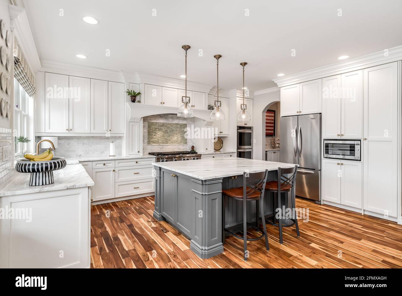 Eine luxuriöse, weiße Küche mit einer Granitplatte und einem gefliesten Backsplash hinter dem Edelstahl KitchenAid Herd. Stockfoto