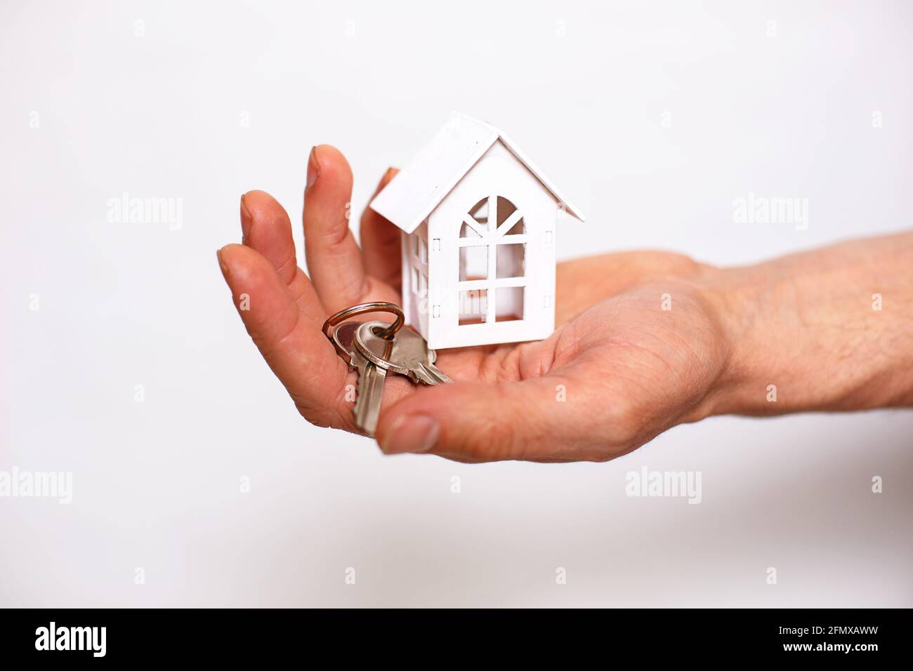 Schlüsselanhänger mit Hausschlüsseln an der Hand eines Mannes auf weißem Hintergrund. Immobilienmakler, Neuhaus Verkauf, Hypothek, Umzug, Banken, Reparatur und Konstruktion Stockfoto