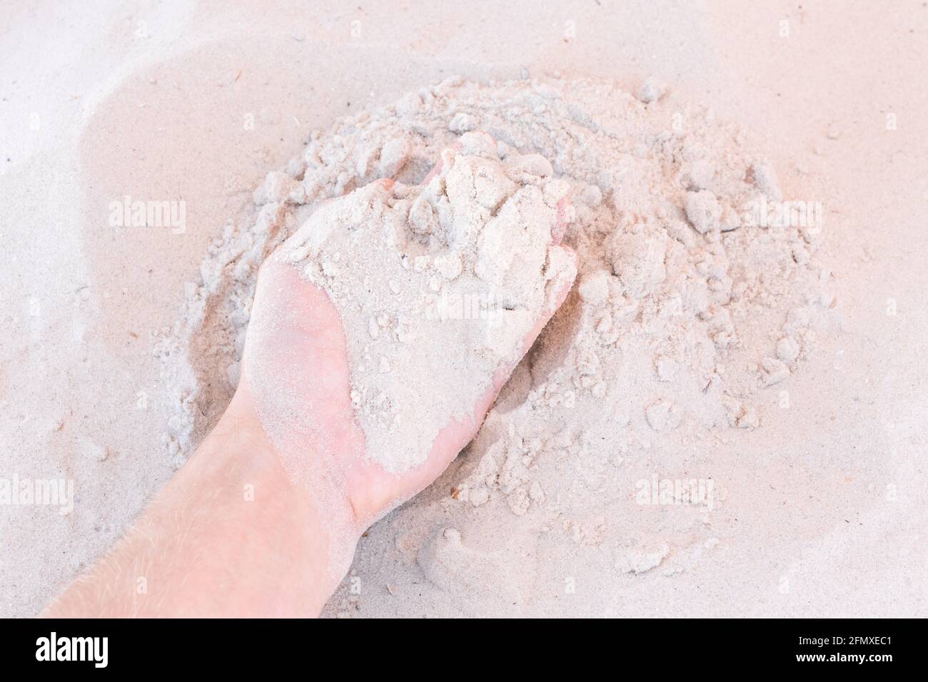 Die Hand des Typen nimmt oder berührt den weißen Strandsand aus nächster Nähe. Stockfoto