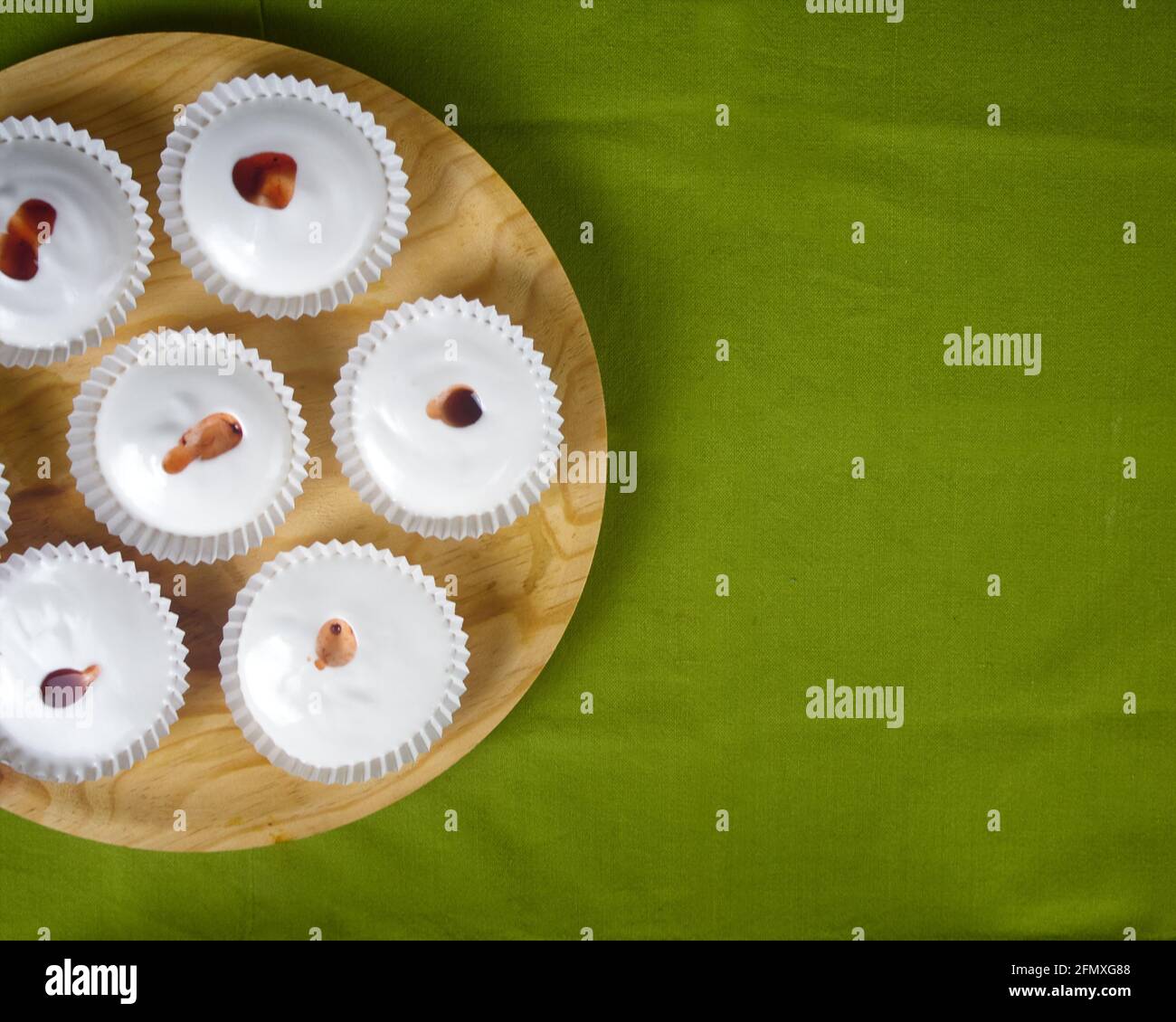 Mehrere rohe französische Dessert-Meringues mit Erdbeersoße auf einer grünen Tischdecke und einem runden Holzteller. Draufsicht Stockfoto