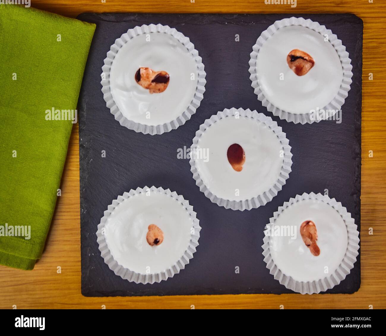 Mehrere rohe französische Dessert-Meringues mit Erdbeersauce, verziert mit einer Serviette auf einem Holztisch und einem schwarzen Schieferbrett. Draufsicht Stockfoto