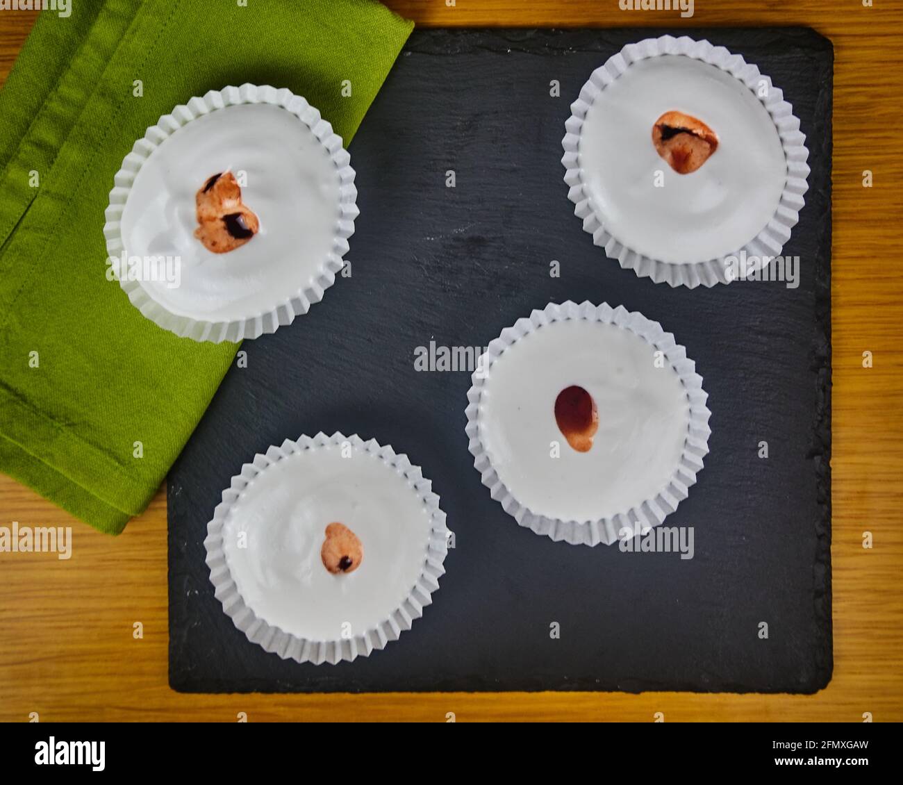 Mehrere rohe französische Dessert-Meringues mit Erdbeersauce, verziert mit einer Serviette auf einem Holztisch und einem schwarzen Schieferbrett. Draufsicht Stockfoto