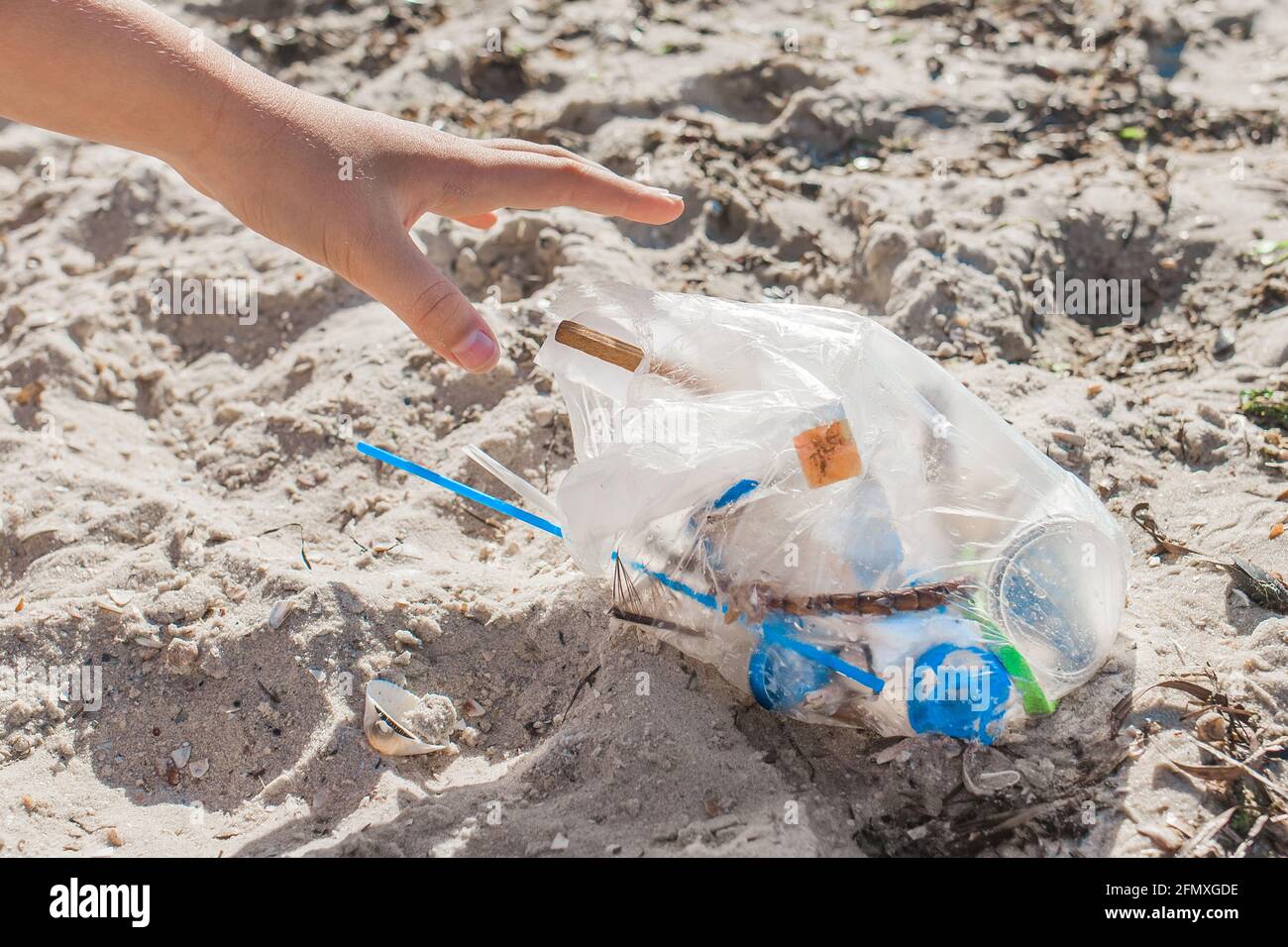 Die Hand des Mädchens reinigt den Müll am Strand. Umweltverschmutzung und Ökologie Konzept. Stockfoto