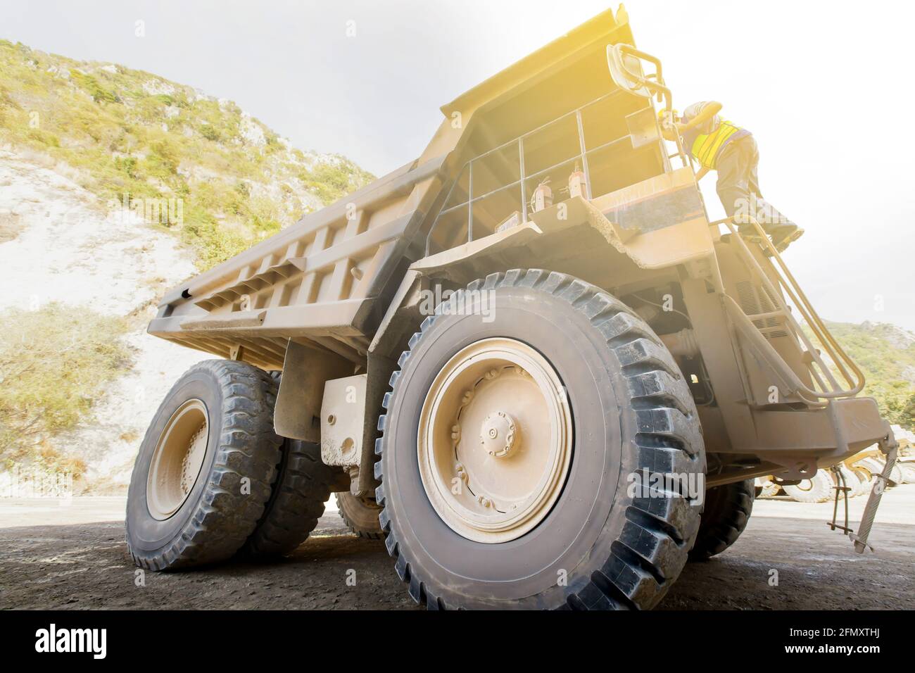 Männlicher Fahrer geht die Treppe eines großen Bergbau-Muldenkipper an einem offenen Grube in der Nähe der Berge. Fokus auf großes Rad. Stockfoto