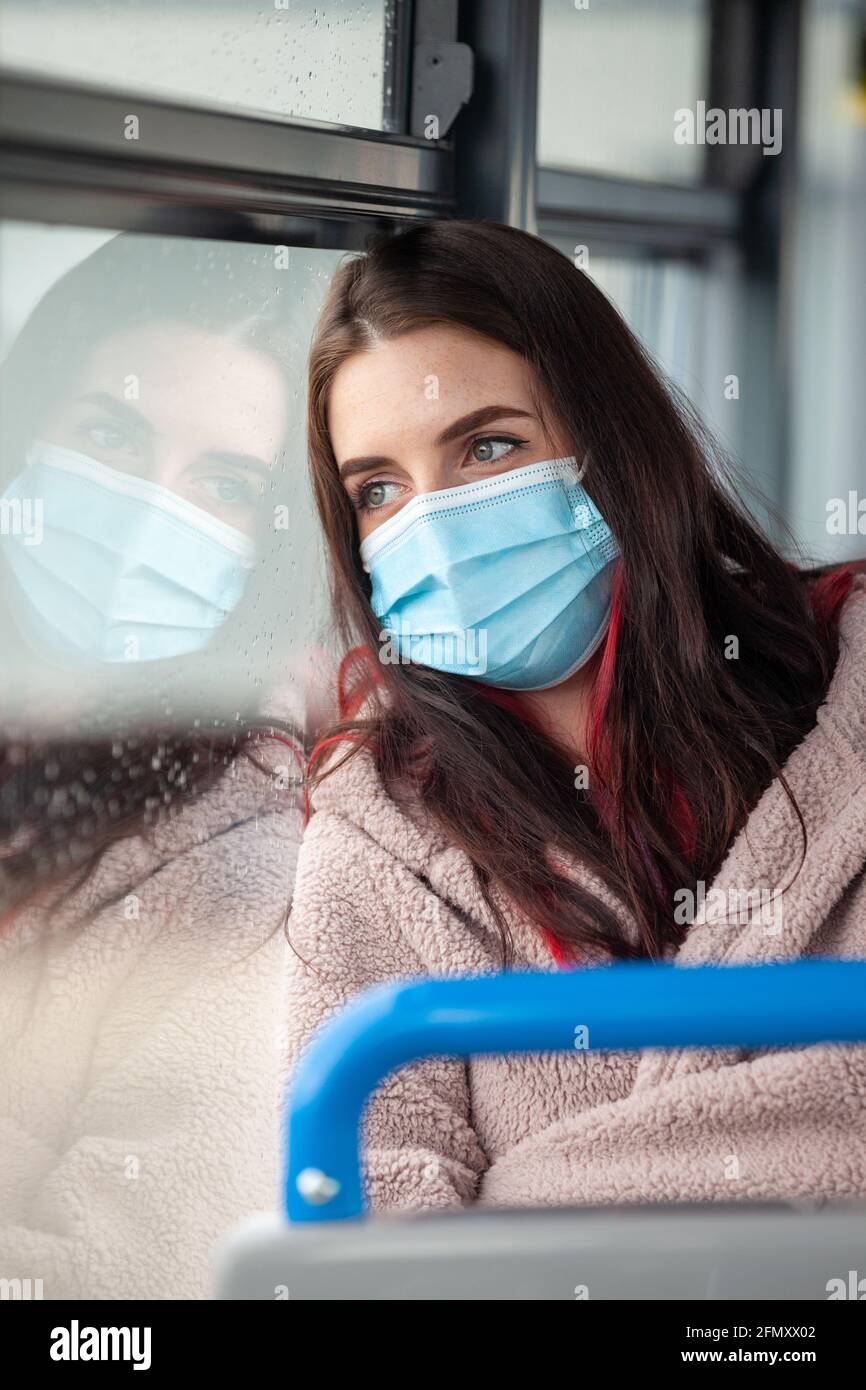 Eine Frau, die in einem Bus mit einer Gesichtsmaske unterwegs ist Und aus einem regnernassen Fenster schauen Stockfoto
