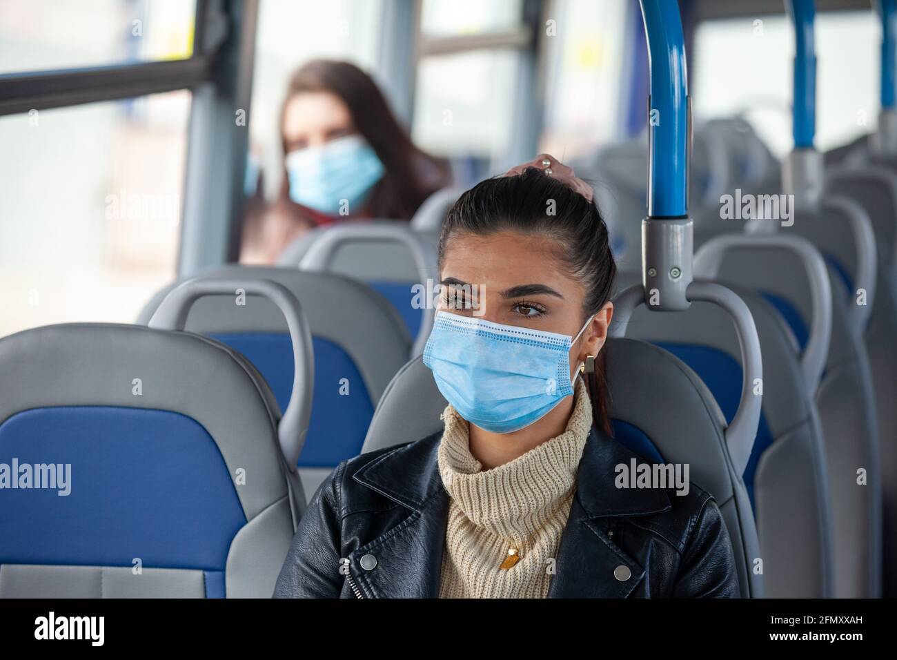 Eine Frau, die in einem Bus mit einer Gesichtsmaske unterwegs ist, und eine andere Frau, die weiter hinten im Bus sitzt. Stockfoto