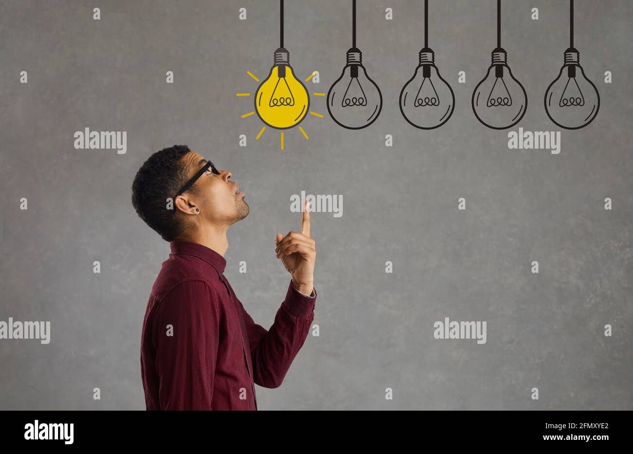 Seitenansicht des jungen schwarzen Geschäftsmannes, der unter mehreren symbolischen wählen kann Idea Glühlampen Stockfoto