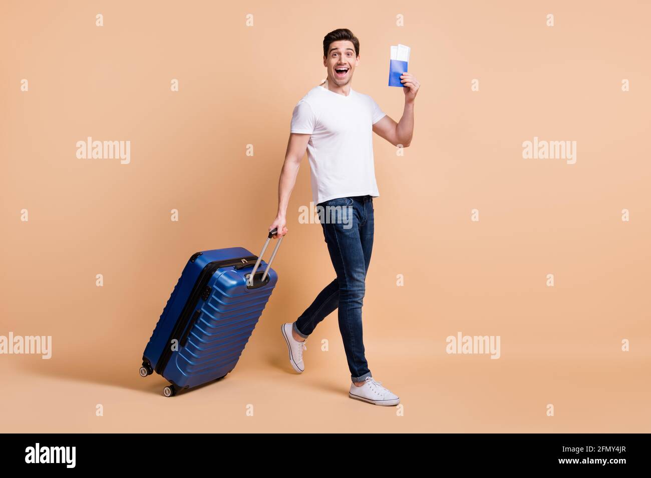 In voller Größe Profilfoto von beeindruckt Brunet Mann gehen halten Tickets Tasche tragen T-Shirt Jeans Sneakers isoliert auf beigem Hintergrund. Stockfoto