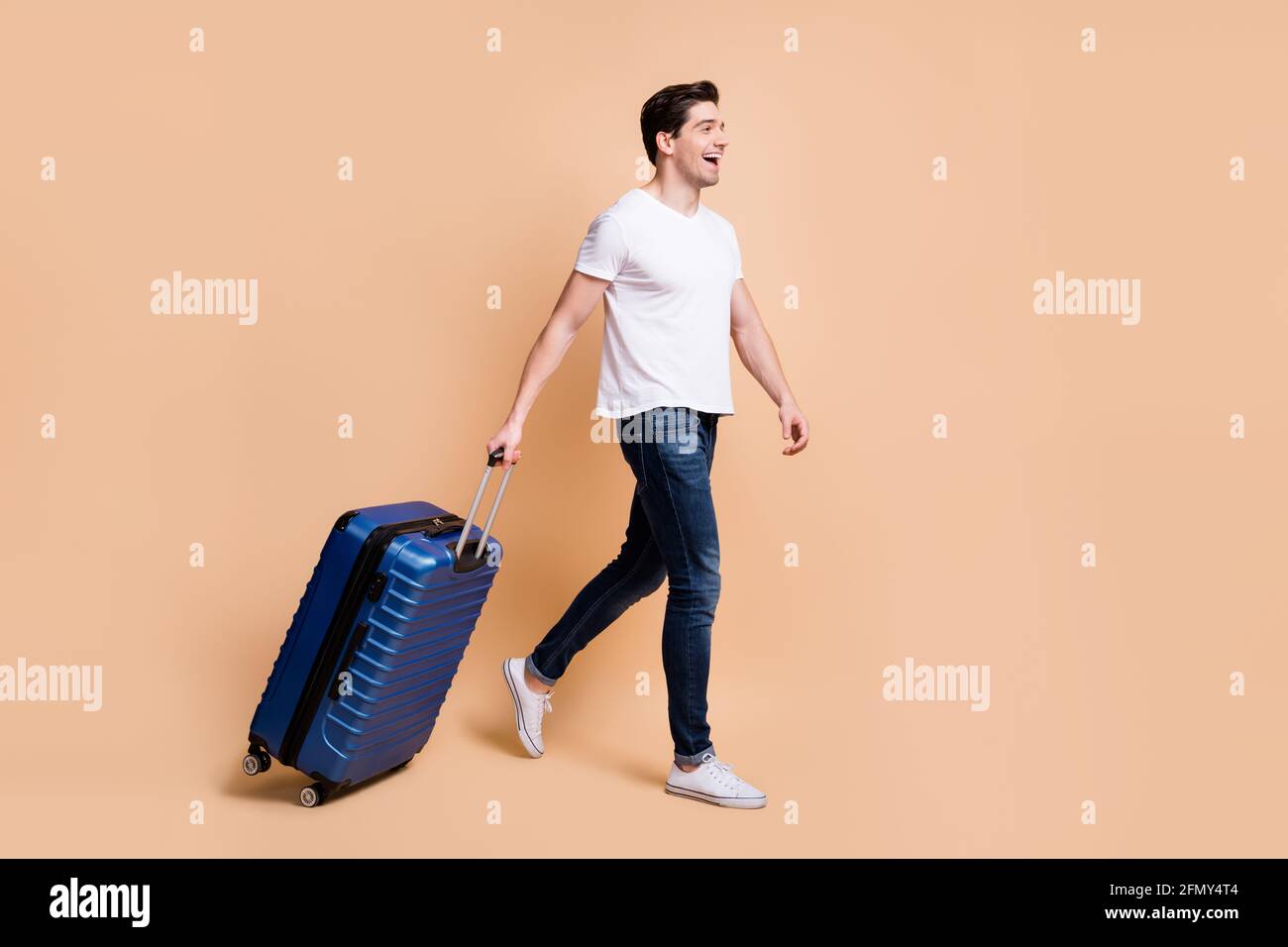 In voller Größe Profilfoto von beeindruckt Brunet Mann gehen halten Tasche tragen T-Shirt Jeans Sneakers isoliert auf beigem Hintergrund. Stockfoto