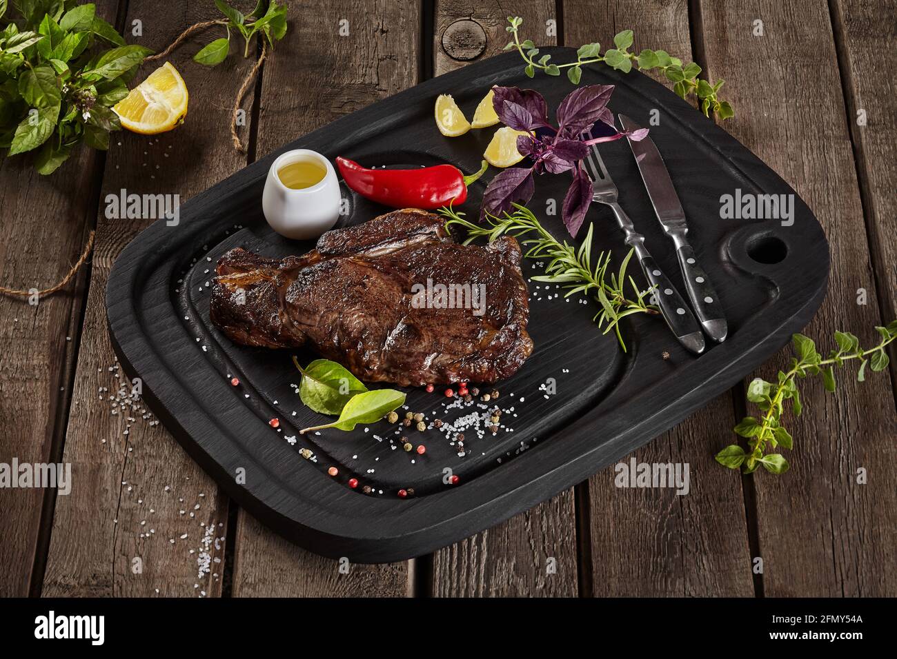 Gegrilltes Kalbssteak mit Gewürzen und Besteck auf Holzhintergrund Stockfoto