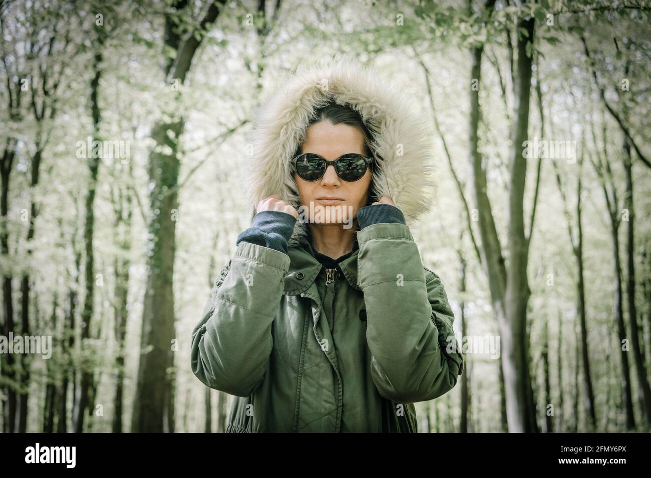 Frau trägt einen Parka Mantel mit der Kapuze oben stehend in einem Wald. Starke weibliche Konzept. Stockfoto