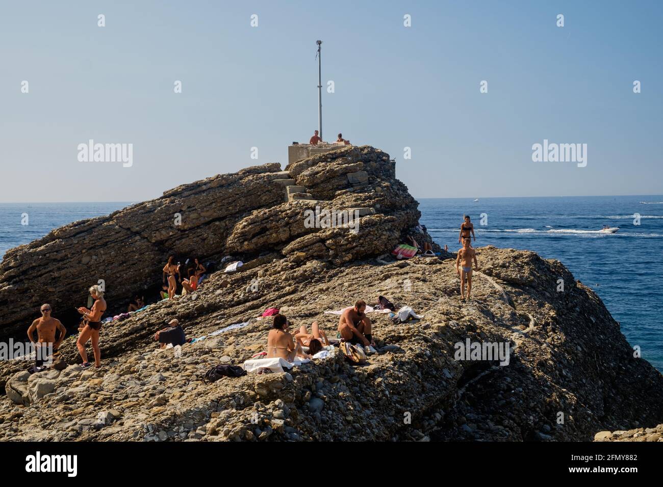 Die Menschen sonnen sich an einem felsigen Strand in Ligurien. Diese einzigartige Lage ist Punta Chiappa in der Nähe von Camogli. Stockfoto