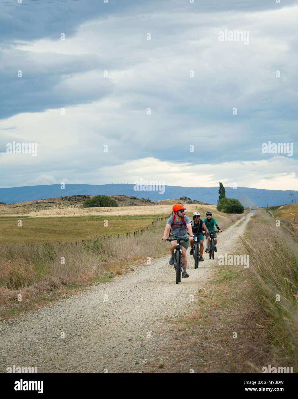Drei Radfahrer fahren auf dem Otago Central Rail Trail unter den flauschigen weißen Wolken, South Island. Vertikales Format. Stockfoto