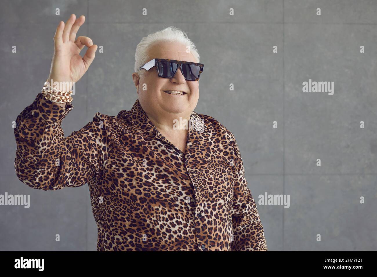 Glücklicher, reicher, molliger älterer Mann mit Leopardenhemd, goldenem Armband und Brille, der eine gute Geste machte Stockfoto