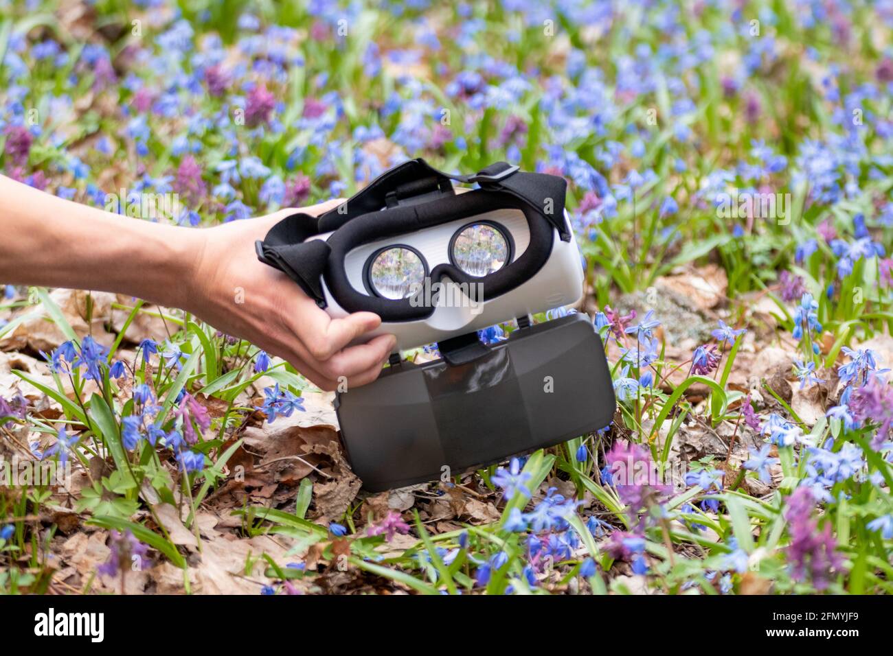 3D Virtual Reality-Headset-Brille mit Handgriff. Blick durch die Linse in frühlingsblauen und violetten Wildblumen. VR Tech-Brille. Optisches System für Stockfoto