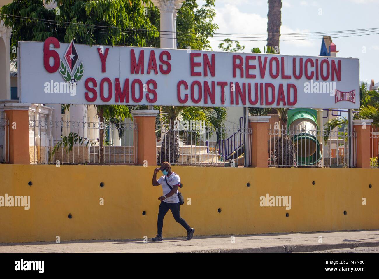 Kubanischer Mann, der an einem Schild mit der Aufschrift „60 Jahre und mehr in der Revolution, Wir sind ein Fortbestand“ in Santiago de Cuba, Kuba, vorbei geht Stockfoto